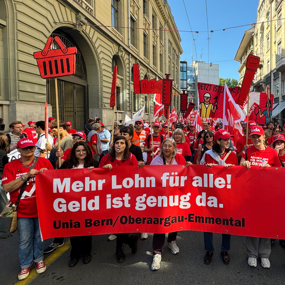 Demonstrationsblock der Unia Bern/Oberaargau-Emmental mit Pfeifen, Fahnen und einem roten Transparent mit der Aufschrift «Mehr Lohn für alle! Geld ist genug da.»